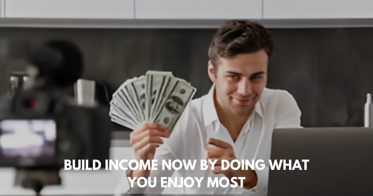 Man holding dollar bills in front of camera while sitting at laptop in kitchen.
