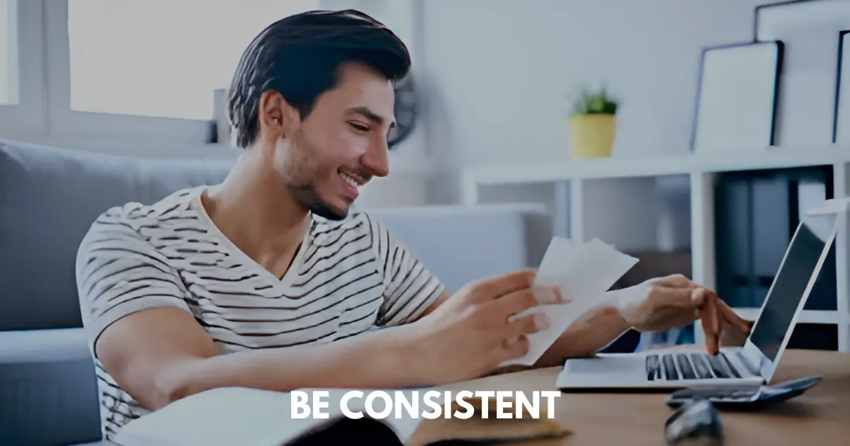 Smiling man typing in laptop while holding a paper in the right hand.